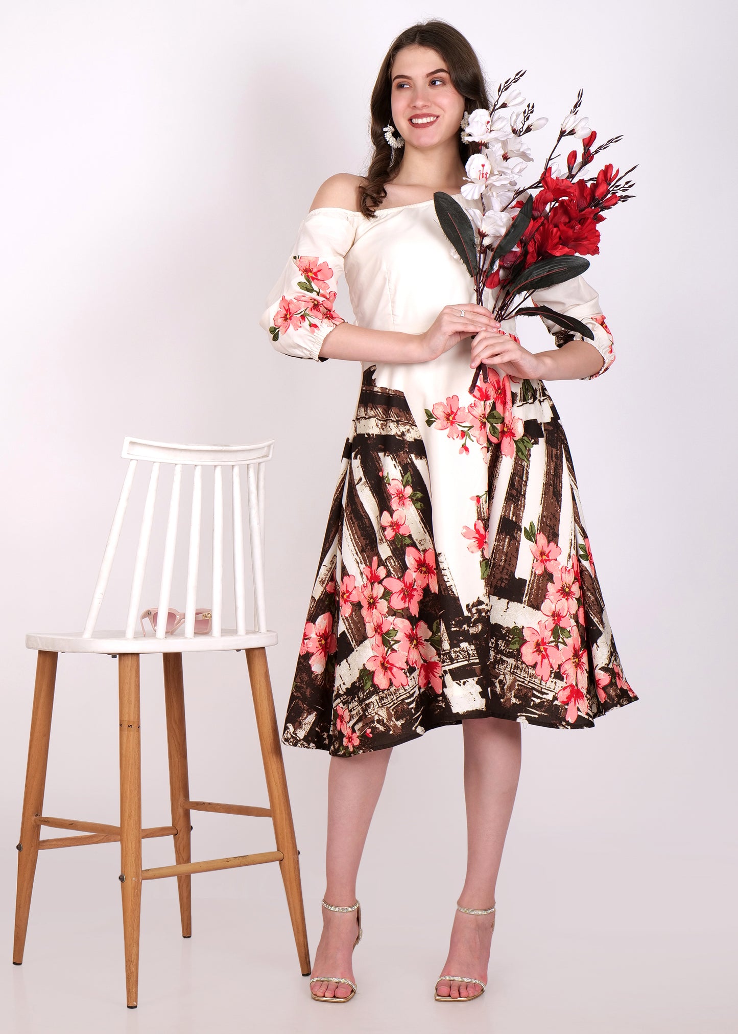 Model in an elegant floral satin dress holding flowers, styled in an off-shoulder design with ruched 3/4 sleeves and a vibrant pink flower print.