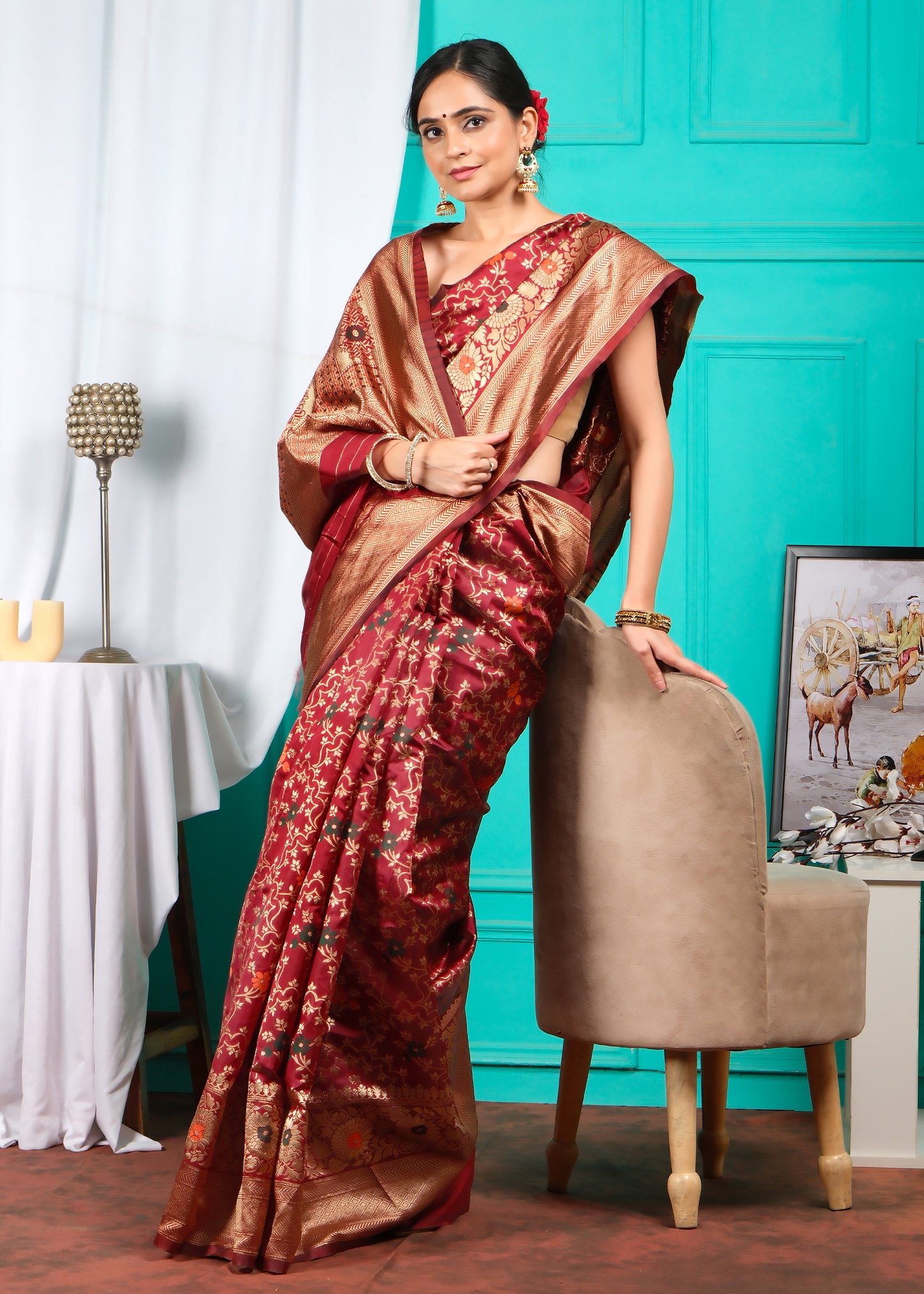 Standing woman in a red Banarasi saree with intricate golden zari work, set against a traditional ethnic decor