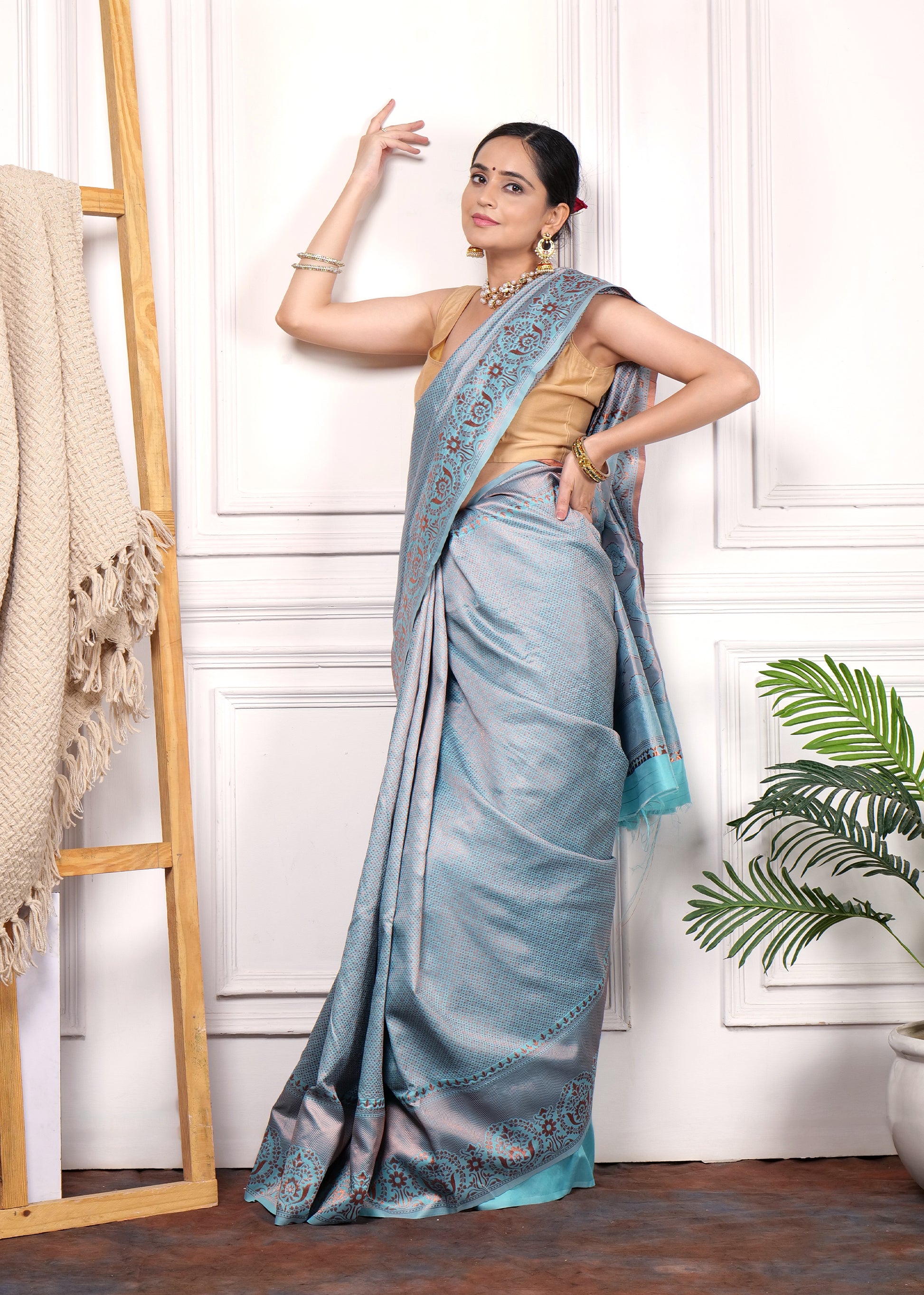 Model in a light blue Banarasi silk saree striking a traditional pose, highlighting the intricate design of the saree with gold jewelry