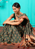 Model gracefully sitting in a green saree with intricate golden floral motifs and a contrasting pallu.