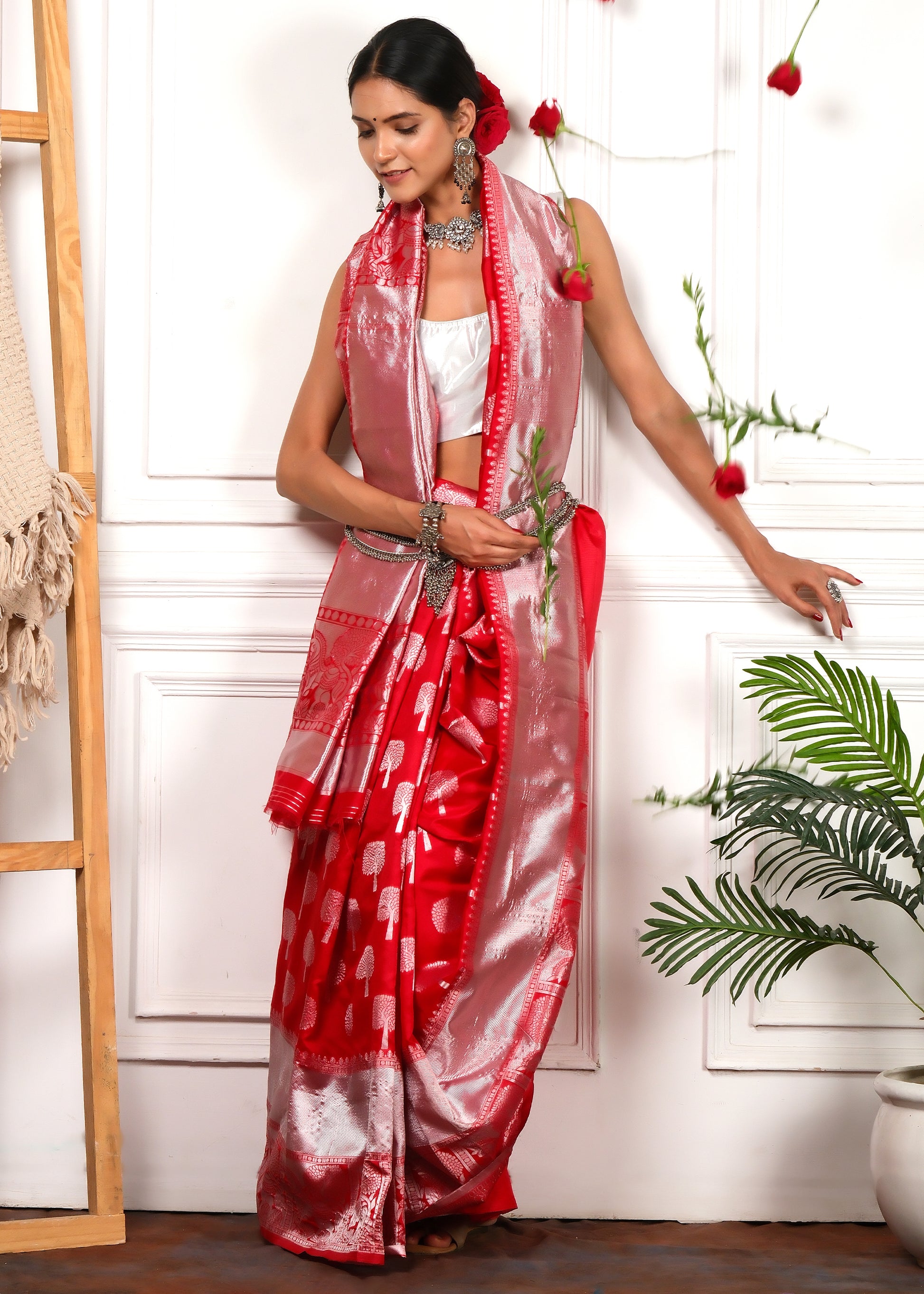 The model in a festive red saree with silver embroidery, surrounded by falling red roses, showcasing a timeless traditional outfit.