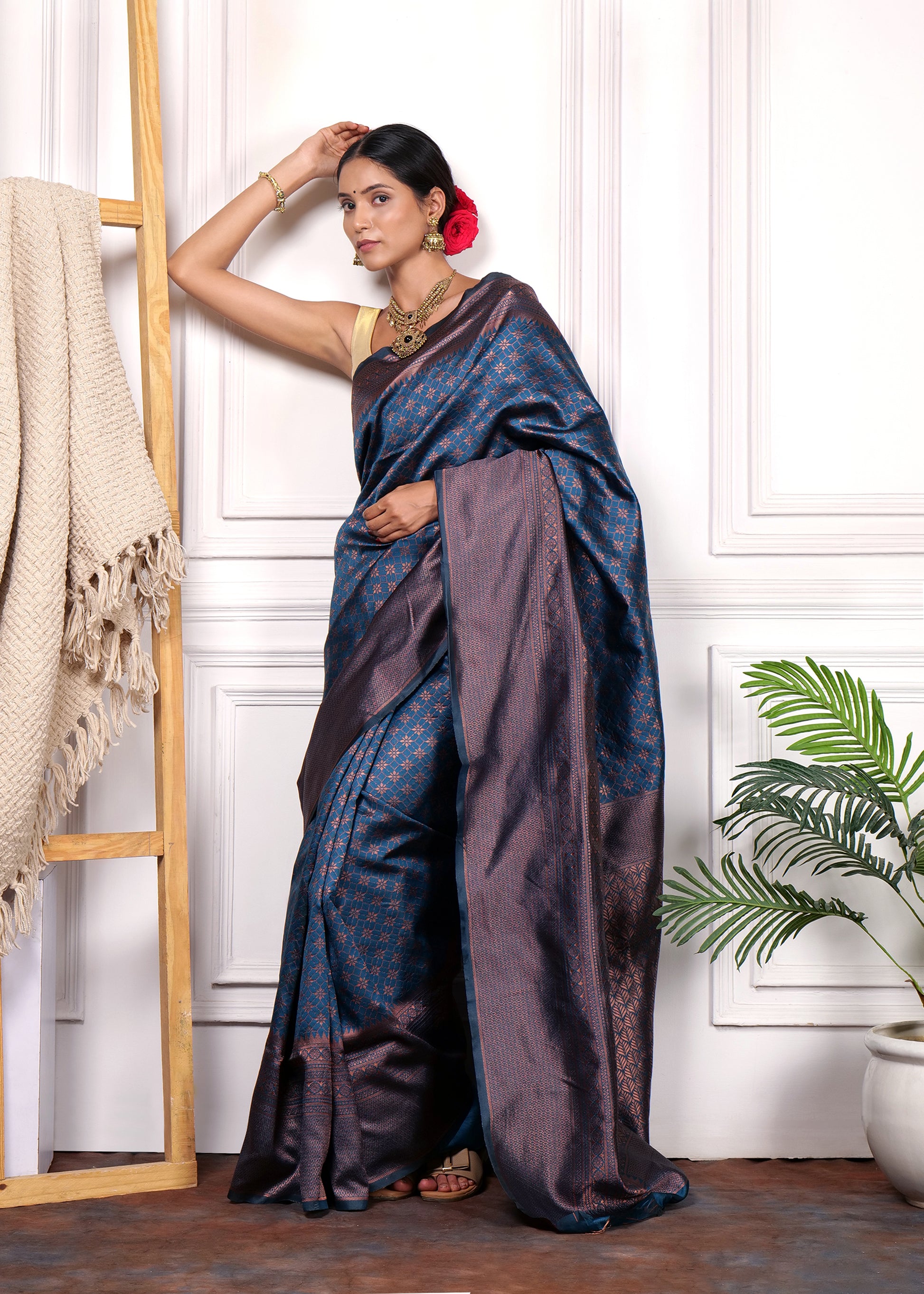 Woman elegantly posing in navy blue and copper Kanjivaram silk saree, styled with antique jewelry and floral hair adornment